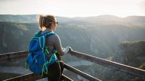 Hiking woman with backpack overlooking river canyon vista during magic hour.
