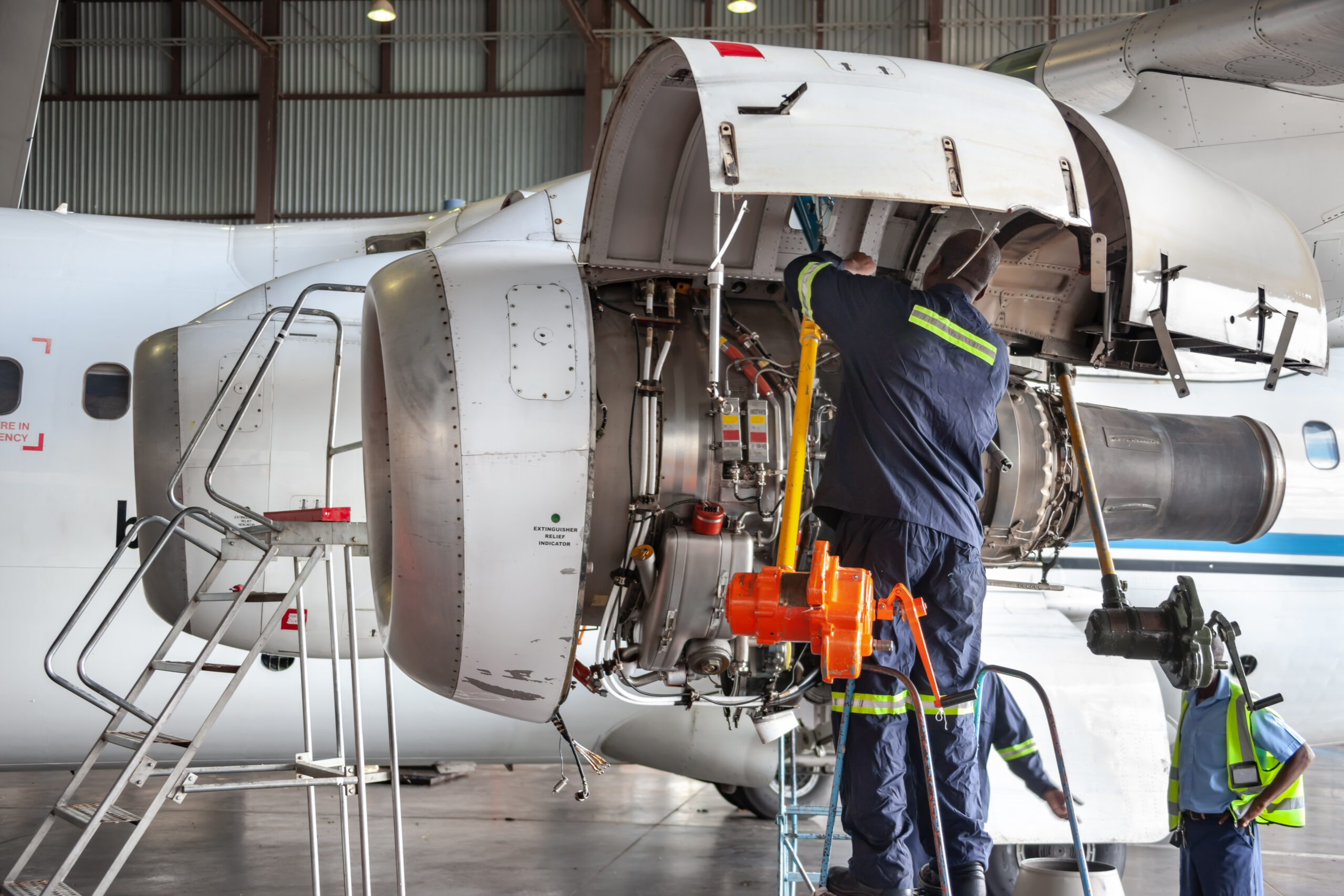 Three airplane mechanics repairing a plane engine in a hangar