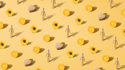 Step and repeat pattern of a wooden heart, and wooden posable figurine, half an orange and a sunlfower